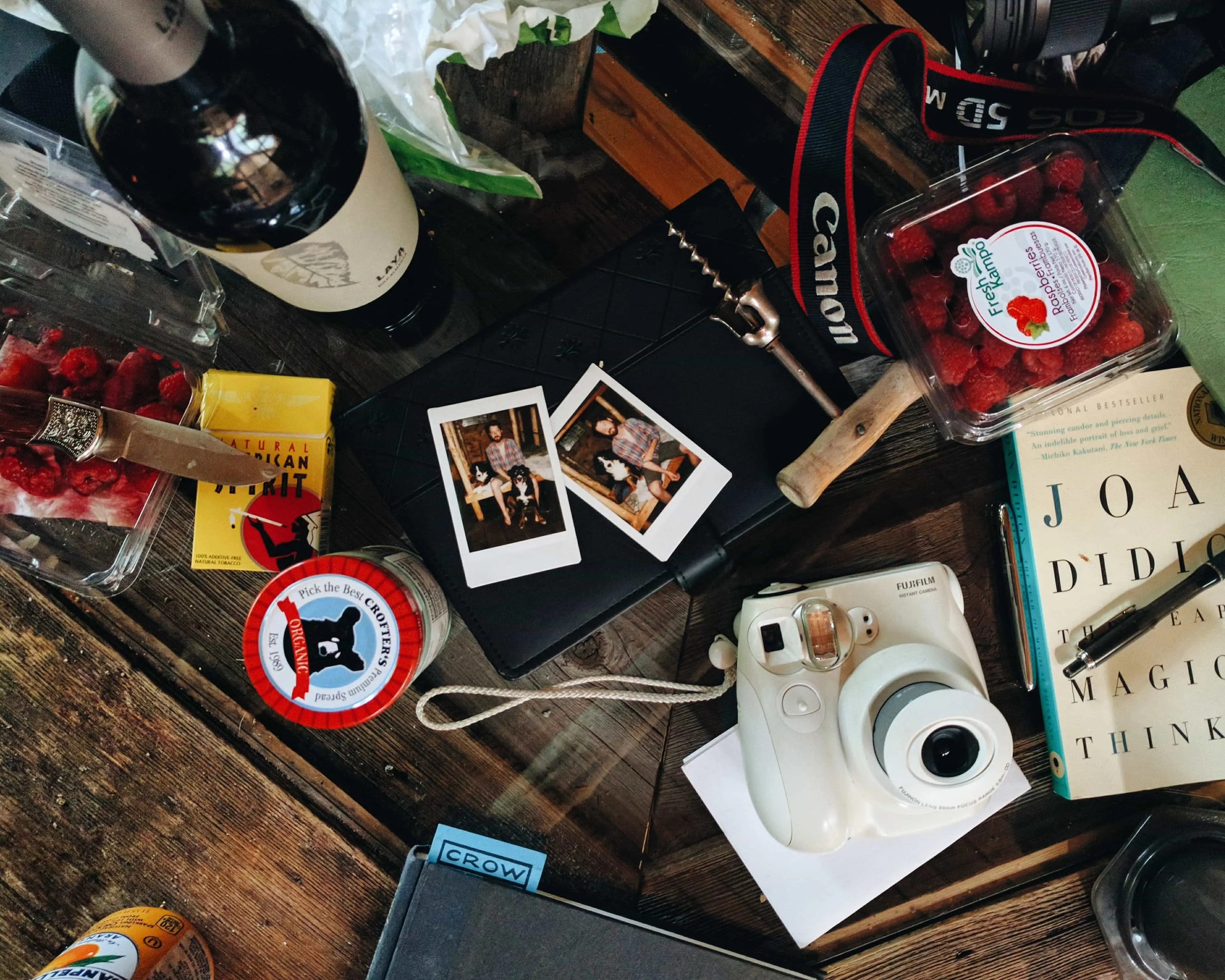 A camera, Polaroids, a notebook and a bottle of wine on a dark wooden table