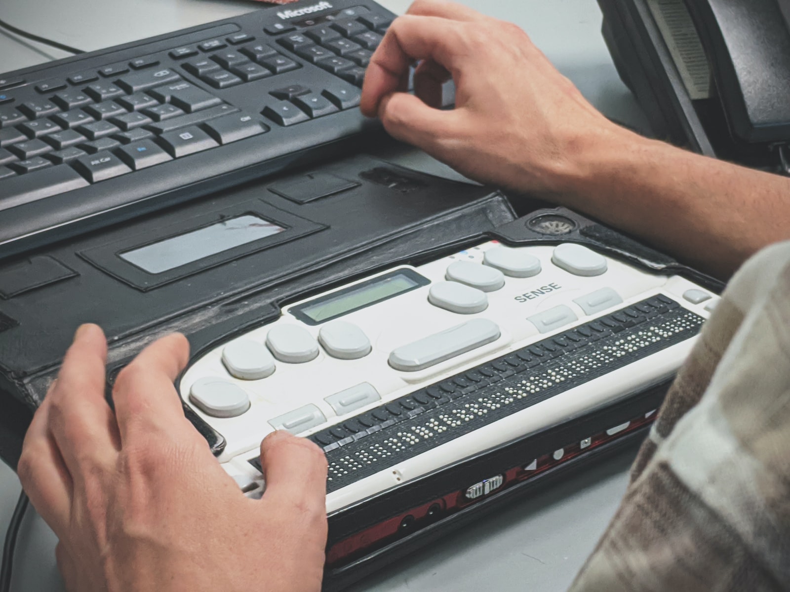 Hands reading a refreshable braille display in front of a keyboard