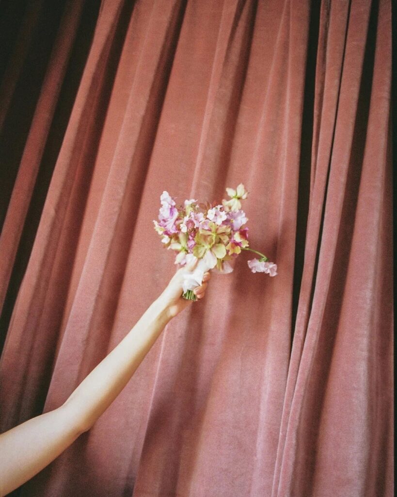 A hand holding a small bouquet against a pink velvet curtain